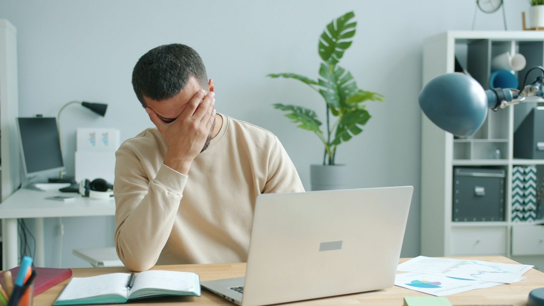 ノートパソコンの前で頭を抱える人 — だらしない自分を責めてしまう様子