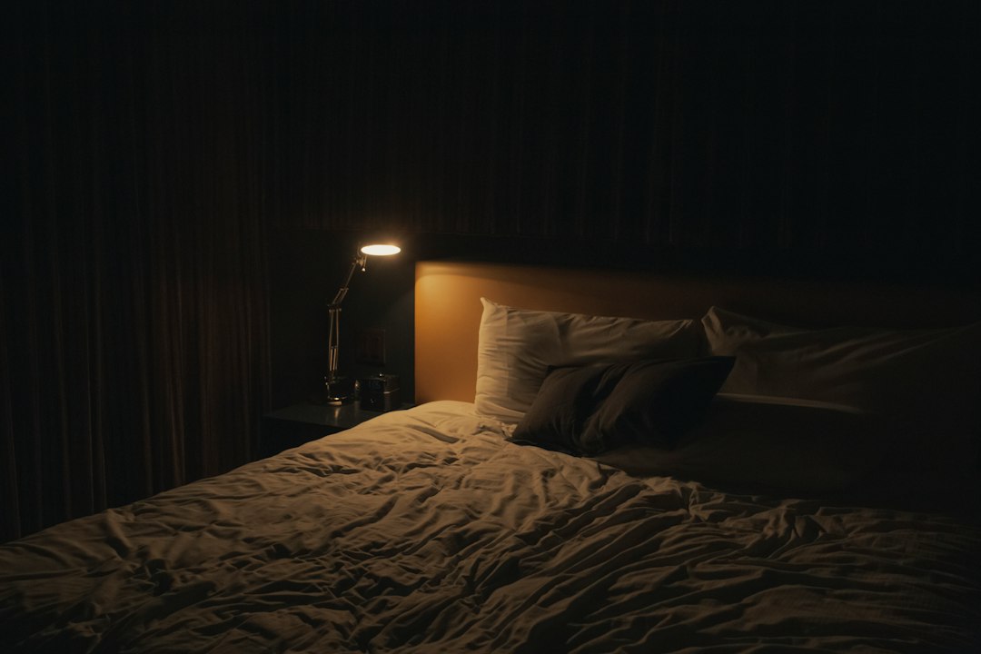 ベッド脇のあかりがともる落ち着いた寝室 — 睡眠の規則性と環境が質を左右する